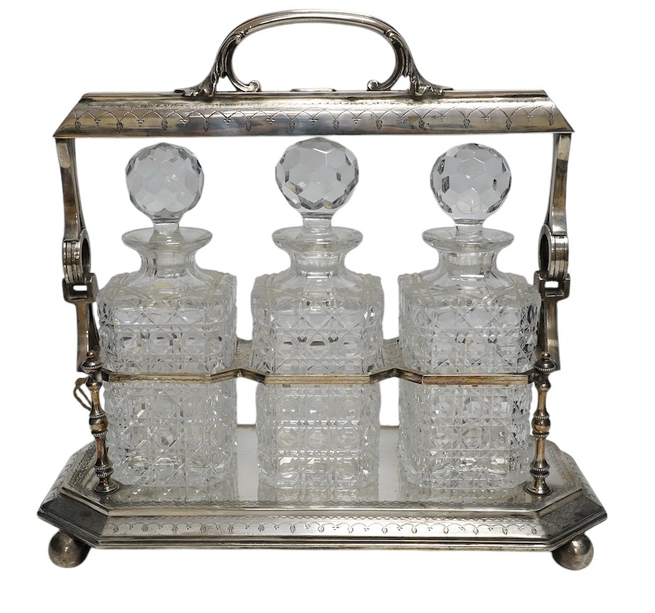 A silver plated three decanter tantalus with unusual duo swing handle locking mechanism, with key, 34cm tall. Condition - fair, a repair to one divider